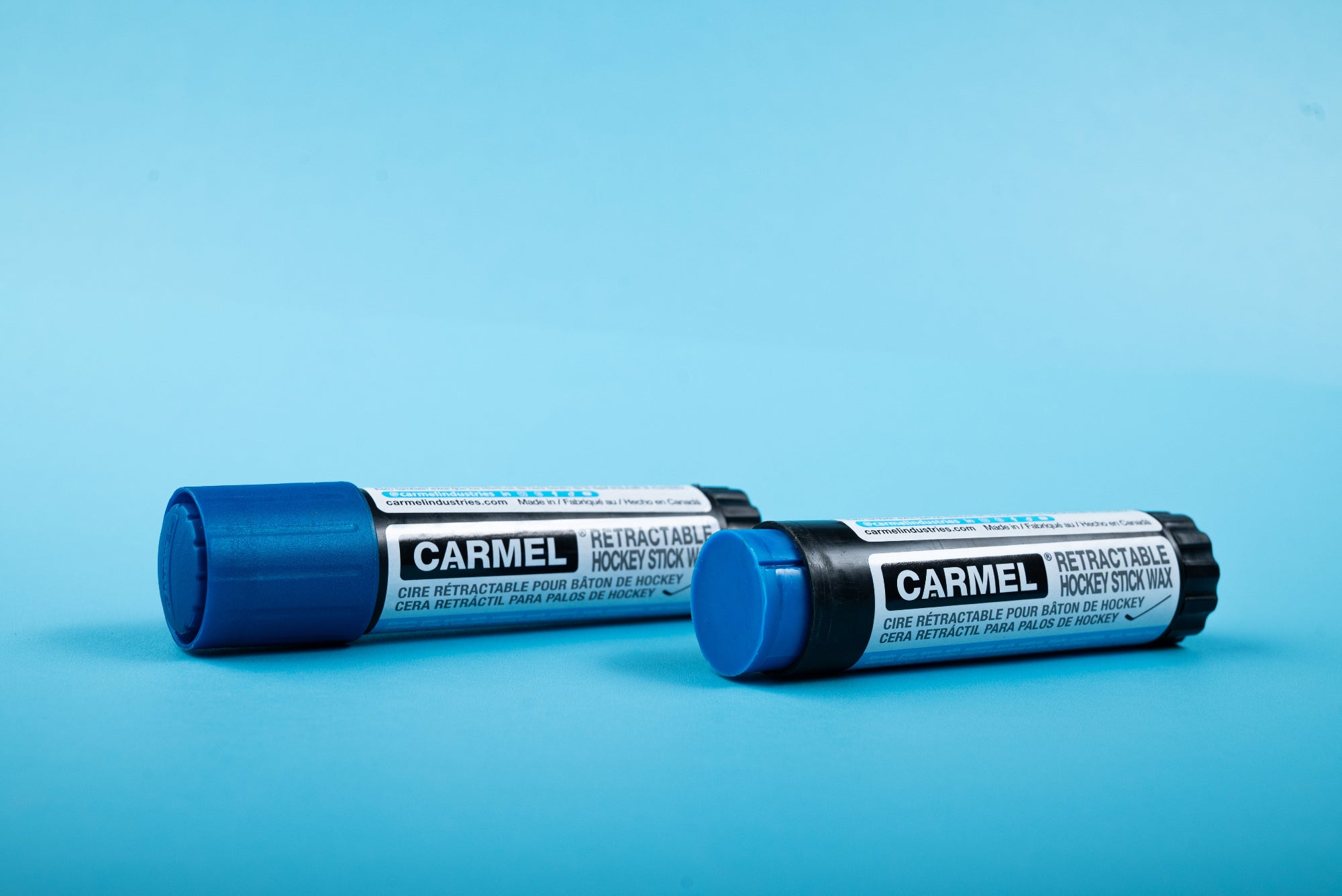 Two Carmel retractable hockey stick wax sticks on a blue background